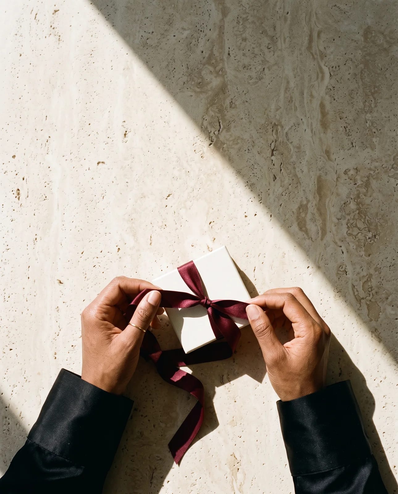 Hands untying the burgundy ribbon on a CHICX gift box on travertine
